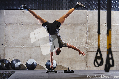 Image of A muscular man in a handstand position, showcasing his exceptional balance and body control while performing a variety of exercises to enhance his overall body stability and strength in a modern gym