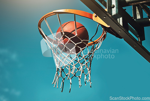 Image of Basketball, goal and target in basket for sports match training on outdoor athletic court. Aim, score and winner with ball dunk in net at competition practice from low angle with blue sky.