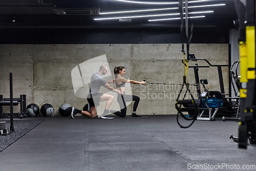 Image of A muscular man assisting a fit woman in a modern gym as they engage in various body exercises and muscle stretches, showcasing their dedication to fitness and benefiting from teamwork and support