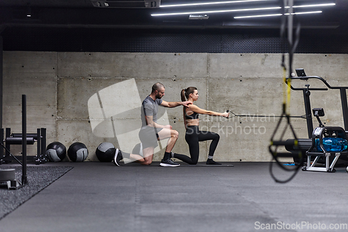 Image of A muscular man assisting a fit woman in a modern gym as they engage in various body exercises and muscle stretches, showcasing their dedication to fitness and benefiting from teamwork and support