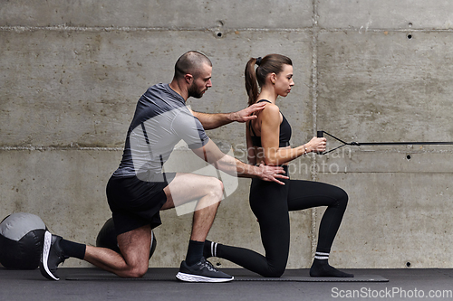 Image of A muscular man assisting a fit woman in a modern gym as they engage in various body exercises and muscle stretches, showcasing their dedication to fitness and benefiting from teamwork and support