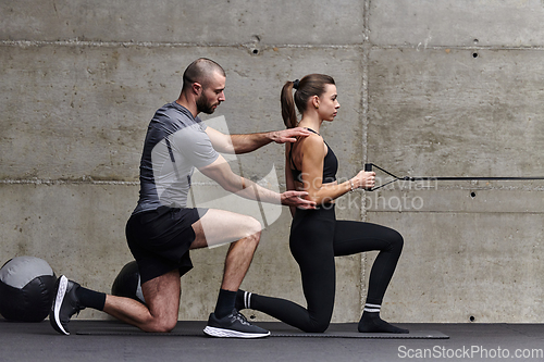 Image of A muscular man assisting a fit woman in a modern gym as they engage in various body exercises and muscle stretches, showcasing their dedication to fitness and benefiting from teamwork and support