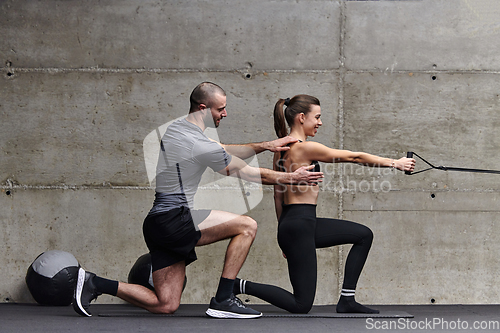 Image of A muscular man assisting a fit woman in a modern gym as they engage in various body exercises and muscle stretches, showcasing their dedication to fitness and benefiting from teamwork and support