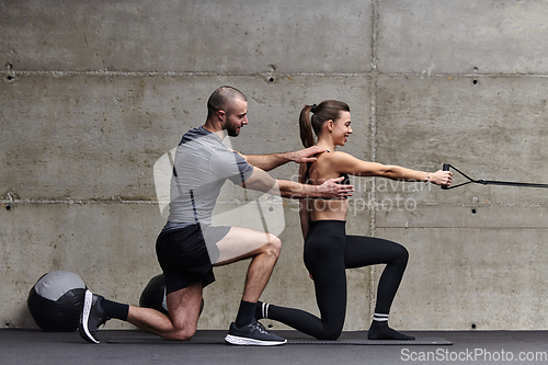 Image of A muscular man assisting a fit woman in a modern gym as they engage in various body exercises and muscle stretches, showcasing their dedication to fitness and benefiting from teamwork and support