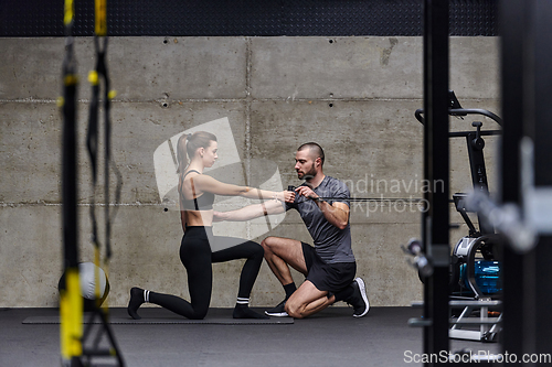 Image of A muscular man assisting a fit woman in a modern gym as they engage in various body exercises and muscle stretches, showcasing their dedication to fitness and benefiting from teamwork and support