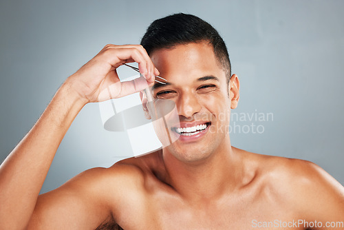 Image of Portrait of a man tweezing his eyebrow with a tweezer in studio with gray background. Happy, smile and young guy plucking brow for hair removal for grooming, cleaning and hygiene routine or self care