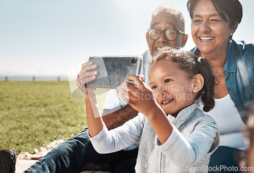 Image of Selfie, phone and girl with grandparents in park for family, happy and technology in summer together. Smile, internet and online with old couple and child relax on grass for bonding and lifestyle