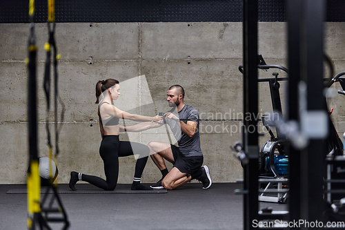 Image of A muscular man assisting a fit woman in a modern gym as they engage in various body exercises and muscle stretches, showcasing their dedication to fitness and benefiting from teamwork and support