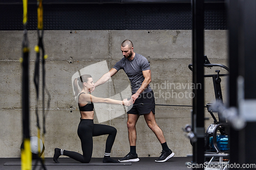 Image of A muscular man assisting a fit woman in a modern gym as they engage in various body exercises and muscle stretches, showcasing their dedication to fitness and benefiting from teamwork and support