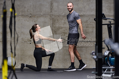 Image of A muscular man assisting a fit woman in a modern gym as they engage in various body exercises and muscle stretches, showcasing their dedication to fitness and benefiting from teamwork and support