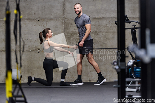 Image of A muscular man assisting a fit woman in a modern gym as they engage in various body exercises and muscle stretches, showcasing their dedication to fitness and benefiting from teamwork and support