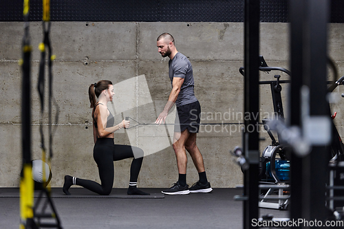 Image of A muscular man assisting a fit woman in a modern gym as they engage in various body exercises and muscle stretches, showcasing their dedication to fitness and benefiting from teamwork and support