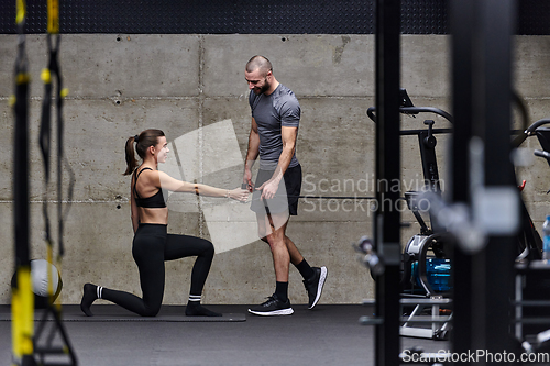 Image of A muscular man assisting a fit woman in a modern gym as they engage in various body exercises and muscle stretches, showcasing their dedication to fitness and benefiting from teamwork and support