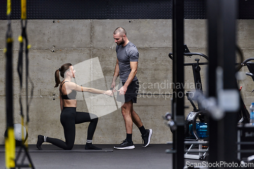 Image of A muscular man assisting a fit woman in a modern gym as they engage in various body exercises and muscle stretches, showcasing their dedication to fitness and benefiting from teamwork and support