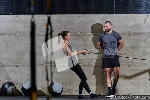 Image of A muscular man assisting a fit woman in a modern gym as they engage in various body exercises and muscle stretches, showcasing their dedication to fitness and benefiting from teamwork and support