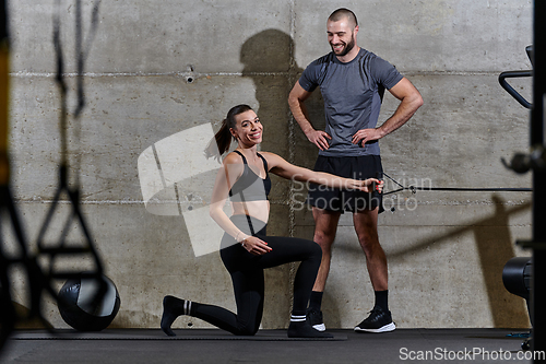 Image of A muscular man assisting a fit woman in a modern gym as they engage in various body exercises and muscle stretches, showcasing their dedication to fitness and benefiting from teamwork and support