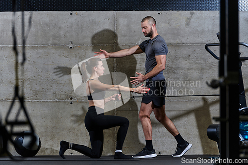 Image of A muscular man assisting a fit woman in a modern gym as they engage in various body exercises and muscle stretches, showcasing their dedication to fitness and benefiting from teamwork and support