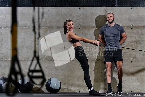 Image of A muscular man assisting a fit woman in a modern gym as they engage in various body exercises and muscle stretches, showcasing their dedication to fitness and benefiting from teamwork and support