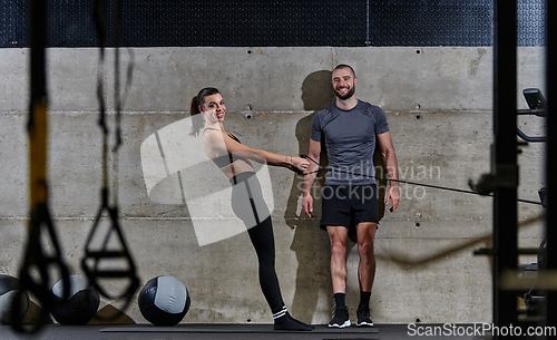 Image of A muscular man assisting a fit woman in a modern gym as they engage in various body exercises and muscle stretches, showcasing their dedication to fitness and benefiting from teamwork and support