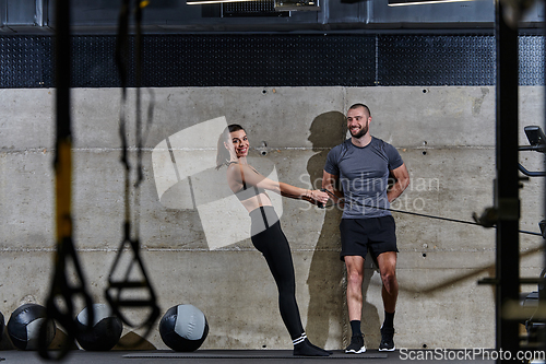 Image of A muscular man assisting a fit woman in a modern gym as they engage in various body exercises and muscle stretches, showcasing their dedication to fitness and benefiting from teamwork and support