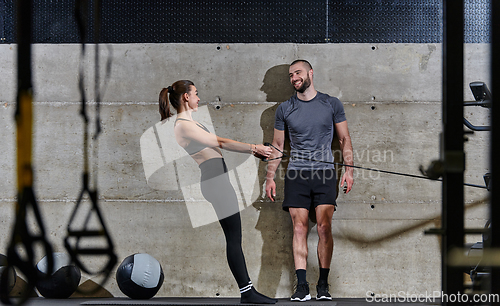 Image of A muscular man assisting a fit woman in a modern gym as they engage in various body exercises and muscle stretches, showcasing their dedication to fitness and benefiting from teamwork and support