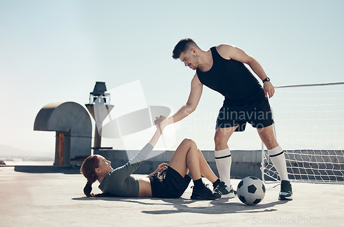 Image of Teamwork, soccer and helping player in sports game, playing football on urban rooftop. Helping hands, inspiration and man giving support to injured woman doing fitness, exercise and training in city