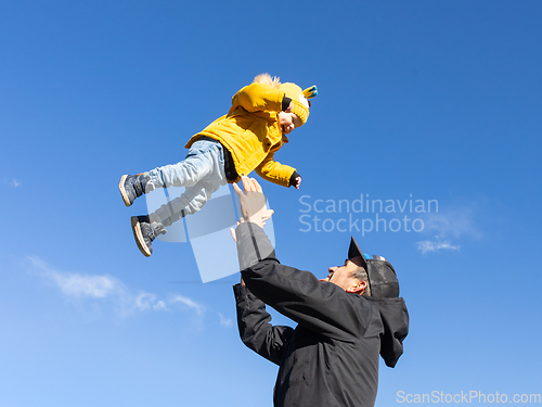 Image of More, more,...dad, that's fun. Happy young father throws his cute little baby boy up in the air. Father's Day, Father and his son baby boy playing and hugging outdoors in nature in fall.