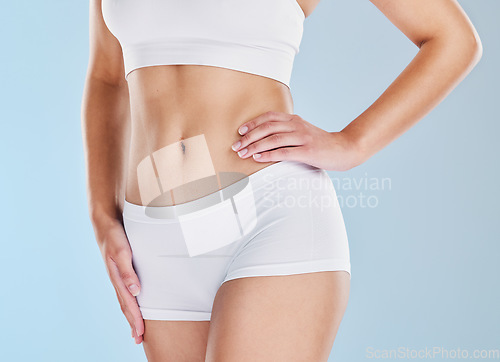 Image of Body, diet and weightloss with a woman in studio on a blue background with her hand on her hip for wellness. Fitness, health and stomach with a model female in underwear for a healthy lifestyle