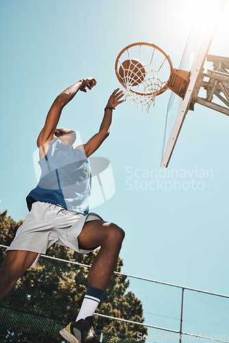 Image of Basketball, sport and man with a goal during a game, professional event or training on an outdoor court in summer. Low view of an athlete in the air to score during sports for fitness and exercise