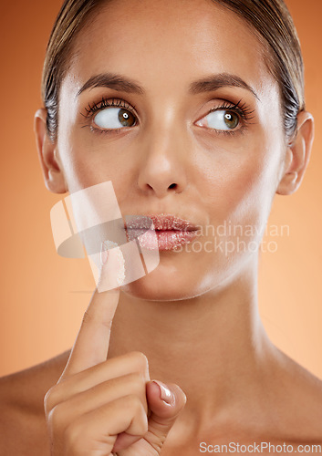 Image of Face, beauty and idea with a model woman applying sugar lip balm her lips in studio on an orange background. Thinking, skin and mouth with an attractive young female posing for cosmetics or wellness