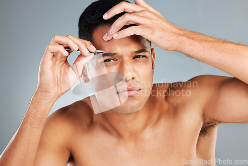 Image of Beauty, grooming and eyebrow tweezers with a man in studio on a gray to remove hair from his eyebrows. Cosmetics, eyes and natural with a handsome young male taking care of his face alone inside