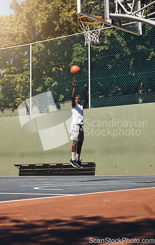 Image of Basketball, jump and athlete scoring a goal during a match or training on an outdoor court. Fitness, sports and man jumping to dunk while playing a game or doing a exercise on a basketball court.