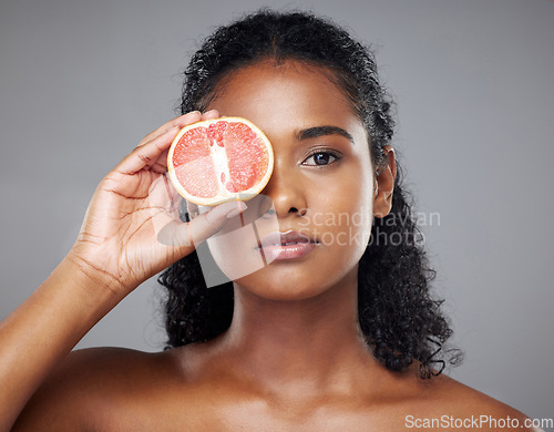 Image of Woman, face skincare or grapefruit for glow, relax wellness health or exfoliate facial on grey studio background. Portrait, Indian beauty model and vitamin c food product in hands for anti aging eyes