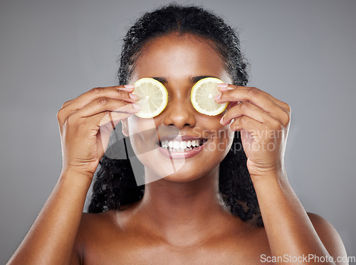 Image of Skincare, portrait and woman with lemon on her eyes for health, beauty and wellness standing in a studio. Happy, smile and face of girl model from Brazil with citrus fruit isolated by gray background