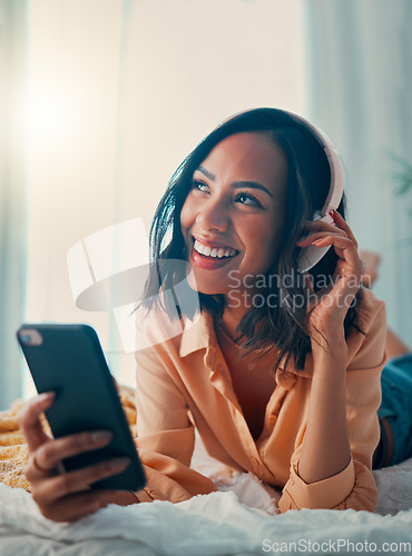 Image of Music, smartphone and relax black woman on bed streaming radio song, wellness podcast or sound. Headphones, digital mobile and happy young girl listening to rock, disco or rap audio in home bedroom