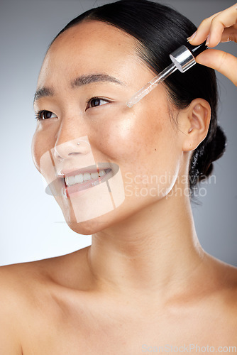 Image of Skincare, face oil and woman with wellness for her skin against a grey studio background. Happy, smile and young Asian model with a facial serum for body healthy, dermatology and a beauty glow