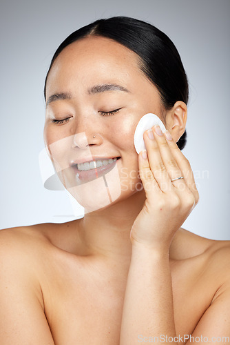 Image of Skincare, asian and woman cleaning face with soft cotton pad for healthy and fresh skin routine. Hygiene, natural and beauty of girl with cosmetics removal swab on grey studio background.