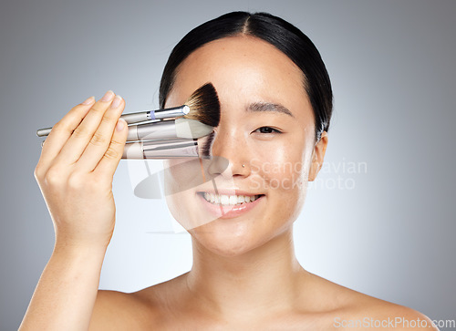 Image of Beauty, makeup and woman with brush for cosmetics against a grey mockup studio background. Portrait of a young, happy and Asian model with a product for facial cosmetic care and mock up space