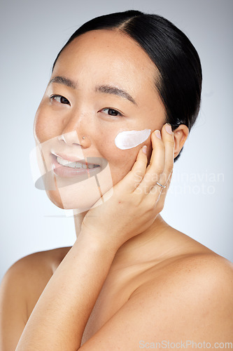 Image of Face, beauty and skincare with an model asian woman in studio on a gray background for wellness. Luxury, health and cosmetics with a young female using an antiaging product or lotion treatment