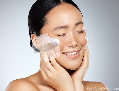 Image of Skincare, beauty and woman with smile using dermatology face cream or cosmetics against studio background. Face of happy, healthy and Asian model doing facial care for wellness and health of skin