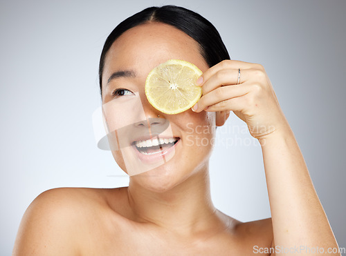 Image of Portrait, happy and woman using lemon for facial skincare cleaning, vitamin c and cosmetic benefits in studio in Tokyo. Smile, fruit and young Asian beauty model cleaning a glowing face for wellness