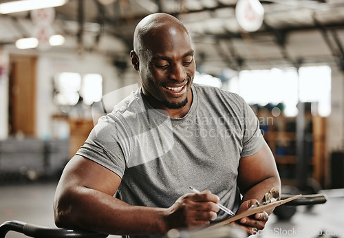 Image of Gym, workout and personal trainer with checklist on clipboard consulting for training sports in gym. Black man of muscular, active and smiling fitness coach writing on health, wellness and exercise