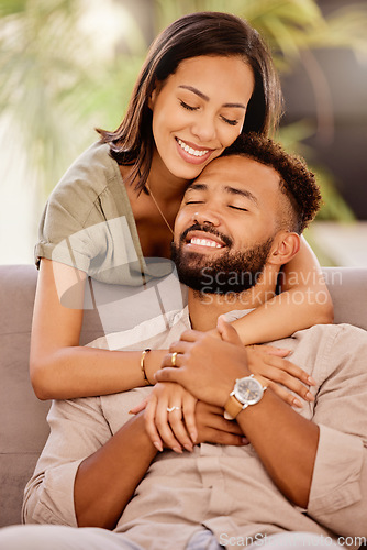 Image of Happy, love and hug with a black couple on the sofa to relax in the living room of the home together. Smile, happy and hugging with a male and female bonding in the lounge of their house for romance