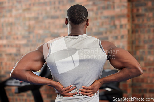 Image of Back pain, fitness and exercise with a sports man suffering from an injury or inflammation during a workout in the gym. Training, health and anatomy with a male athlete struggling with muscle strain