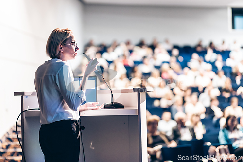 Image of Female speaker giving a talk on corporate business conference. Unrecognizable people in audience at conference hall. Business and Entrepreneurship event.