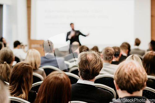 Image of Speaker giving a talk in conference hall at business event. Rear view of unrecognizable people in audience at the conference hall. Business and entrepreneurship concept.