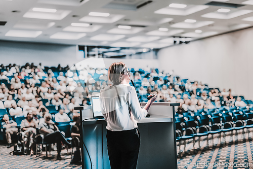 Image of Female speaker giving a talk on corporate business conference. Unrecognizable people in audience at conference hall. Business and Entrepreneurship event.