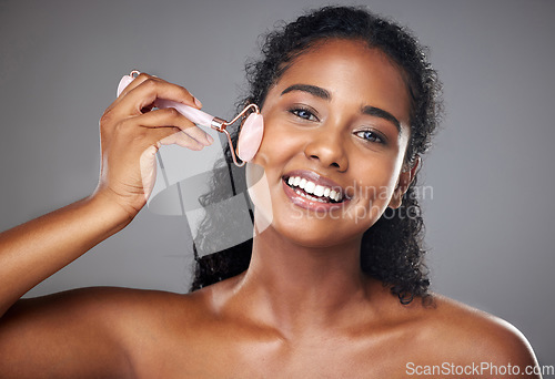 Image of Skincare, portrait and woman with a face roller for wellness, beauty and skin routine in studio. Happy, smile and girl model from Brazil with rose quartz cosmetic tool for self care facial treatment.