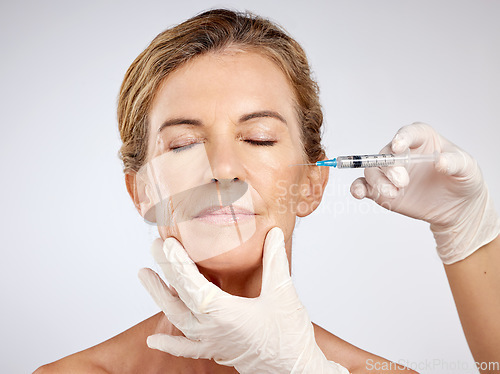 Image of Needle, surgery and face with mature woman getting an injection in her cheek for beauty, skincare and medicine in studio on a blue background. Filler, product and cosmetics with a female model inside