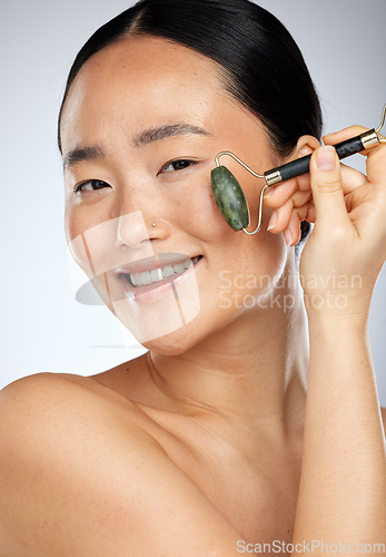 Image of Asian woman, cosmetics and facial roller for wellness, skincare and smooth face with studio background. Young female, girl and anti aging for natural beauty, smile and happy for health and body care.